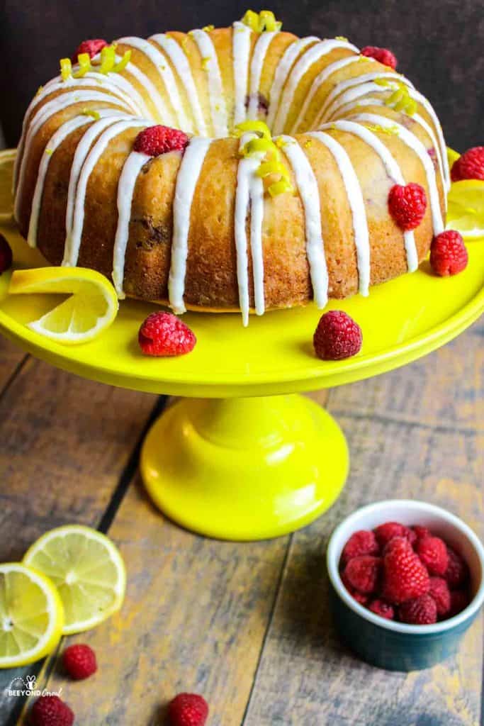 lemon raspberry bundt cake on a yellow cakestand with fresh fruits for garnish