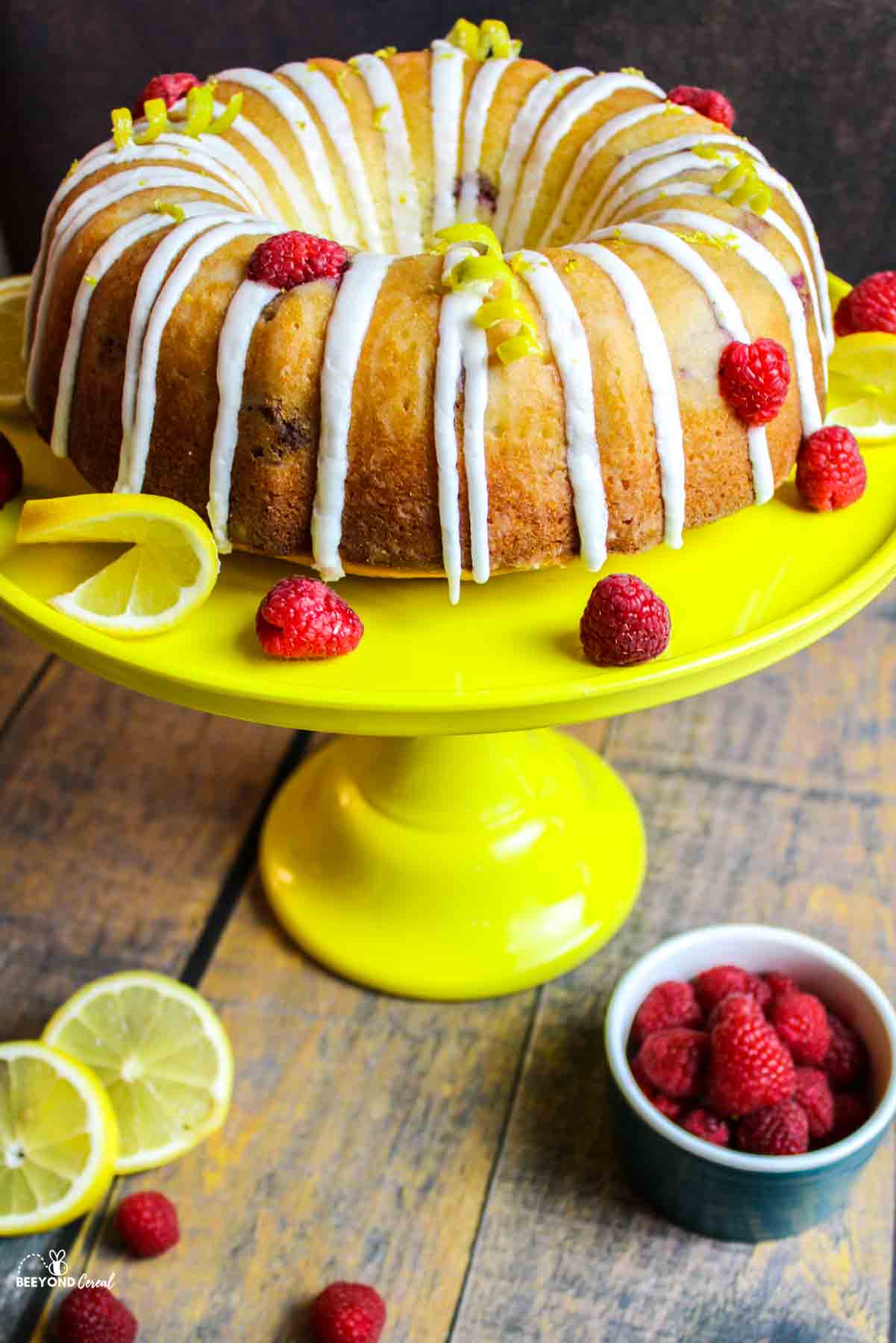 lemon raspberry bundt cake on a yellow cakestand with fresh fruits for garnish.