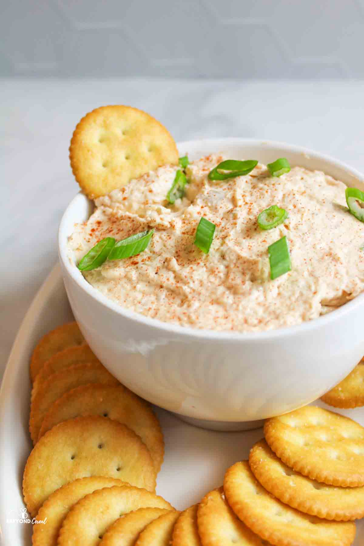 a bowl of pink colored trout dip with a cracker in it and more arranged around it