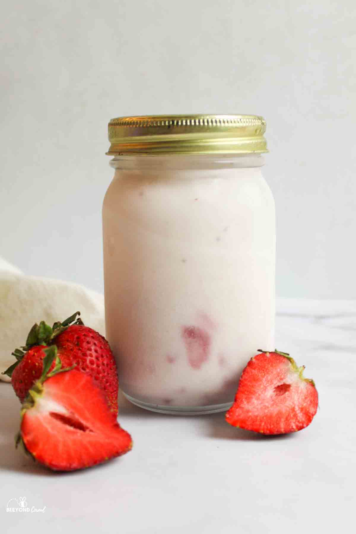 a sealed jar full of strawberry ice cream with fresh strawberries around it