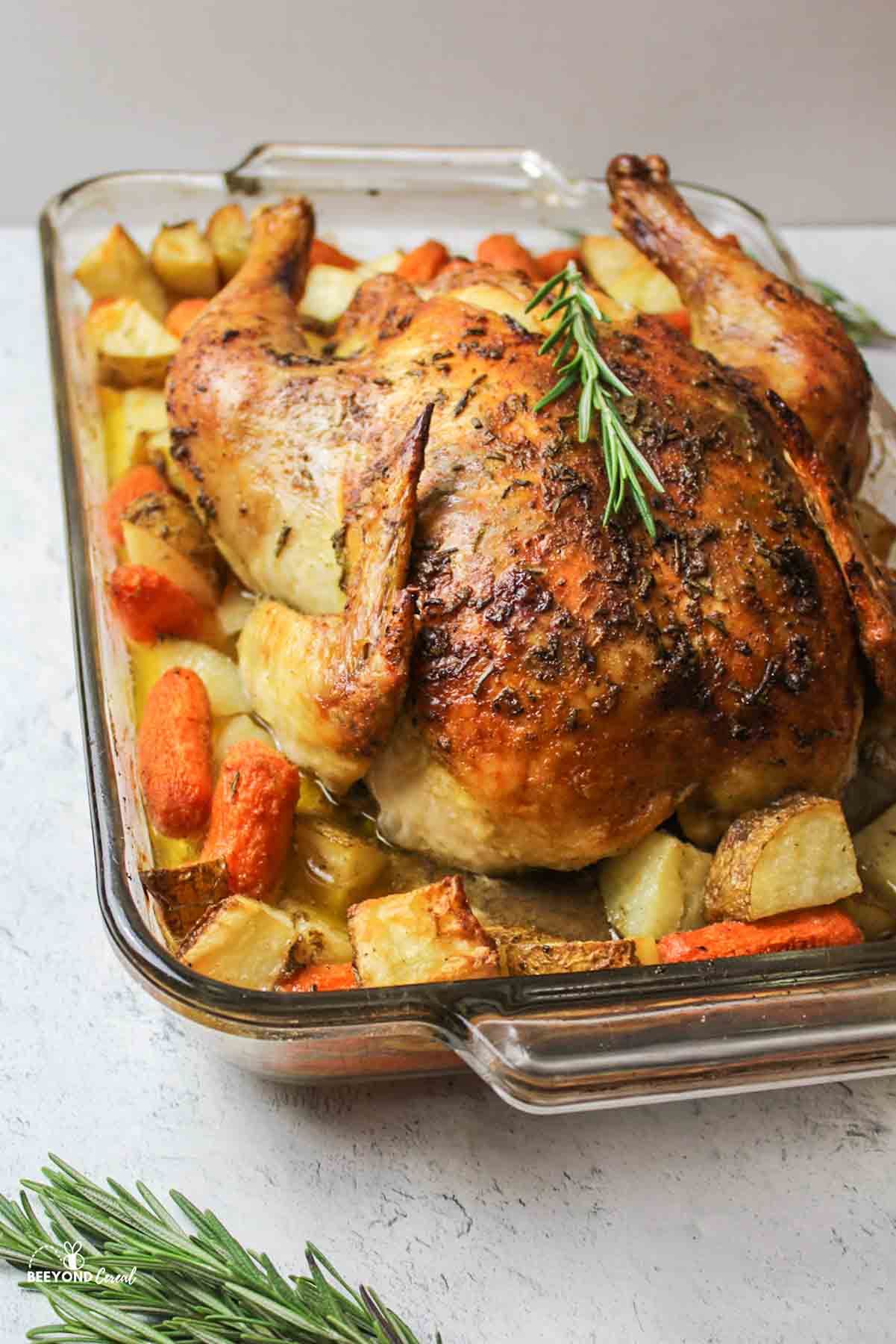 baked whole chicken in a dish with potatoes and carrots.