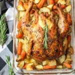 whole roasted chicken in a baking dish with potatoes and carrots