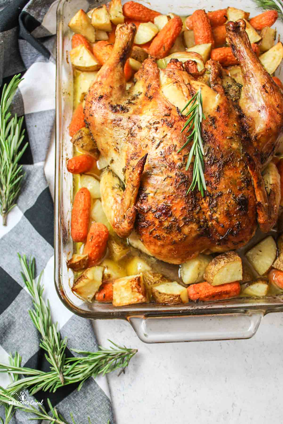 baked chicken, potatoes and carrots in a dish with fresh rosemary around it.