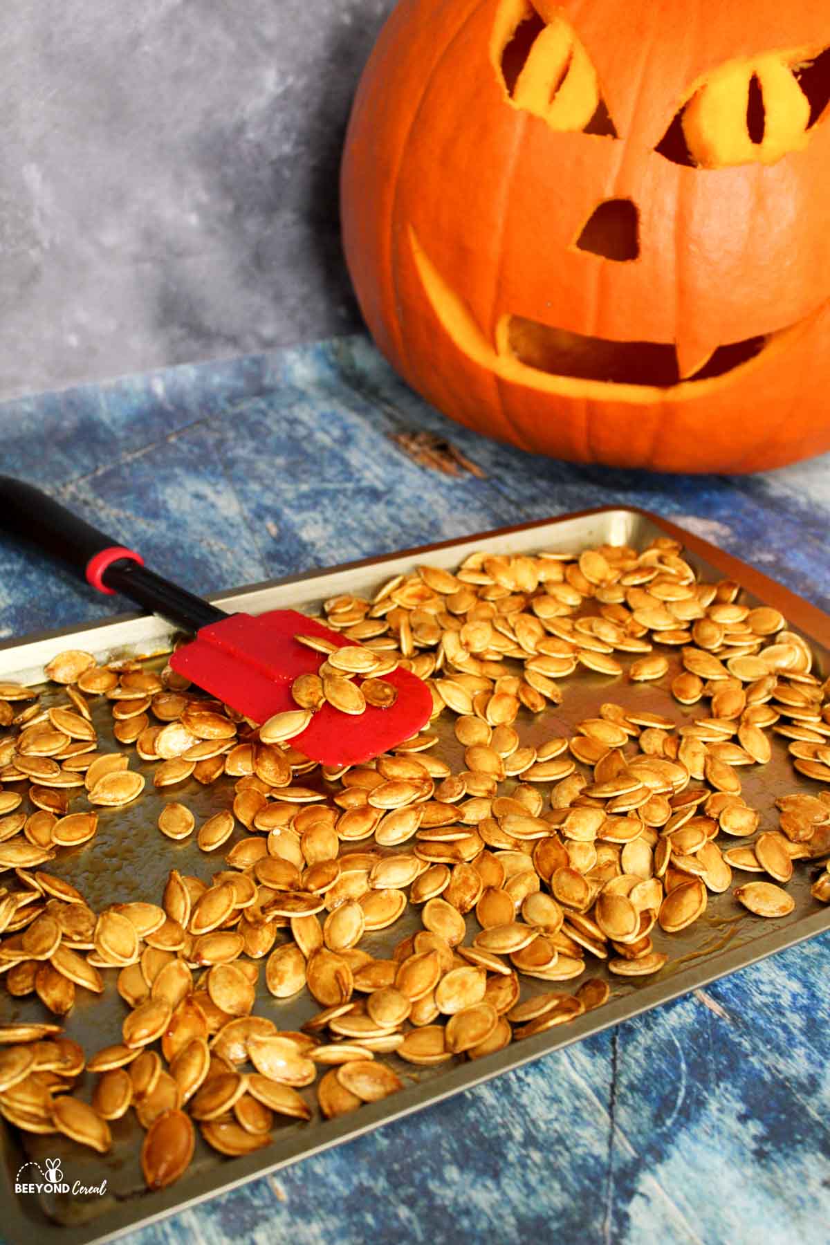 honey roasted pumpkin seeds on a baking sheet with a jack o lantern to the side