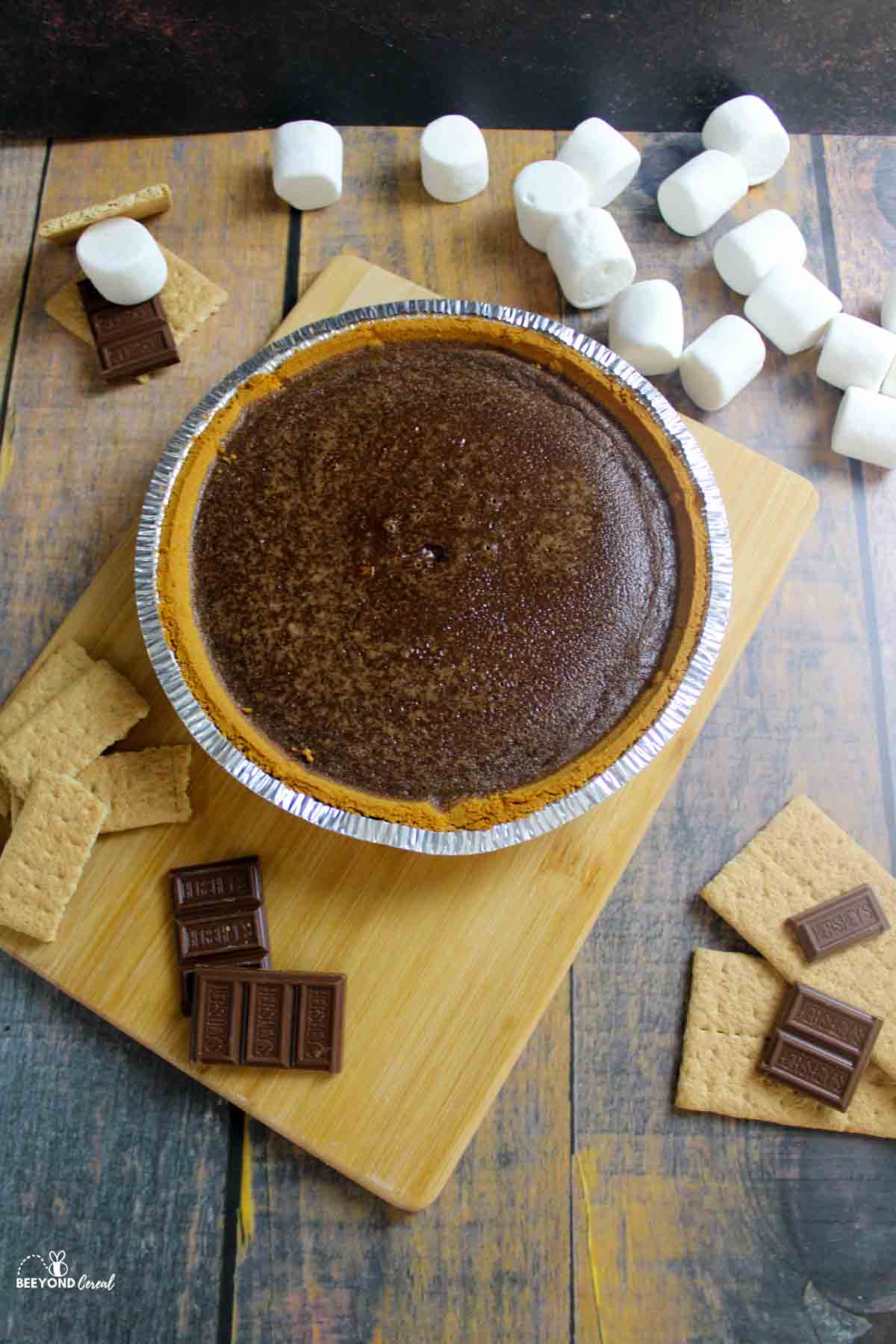 a baked chocolate pie surrounded by marshmallows, chocolate and graham crackers