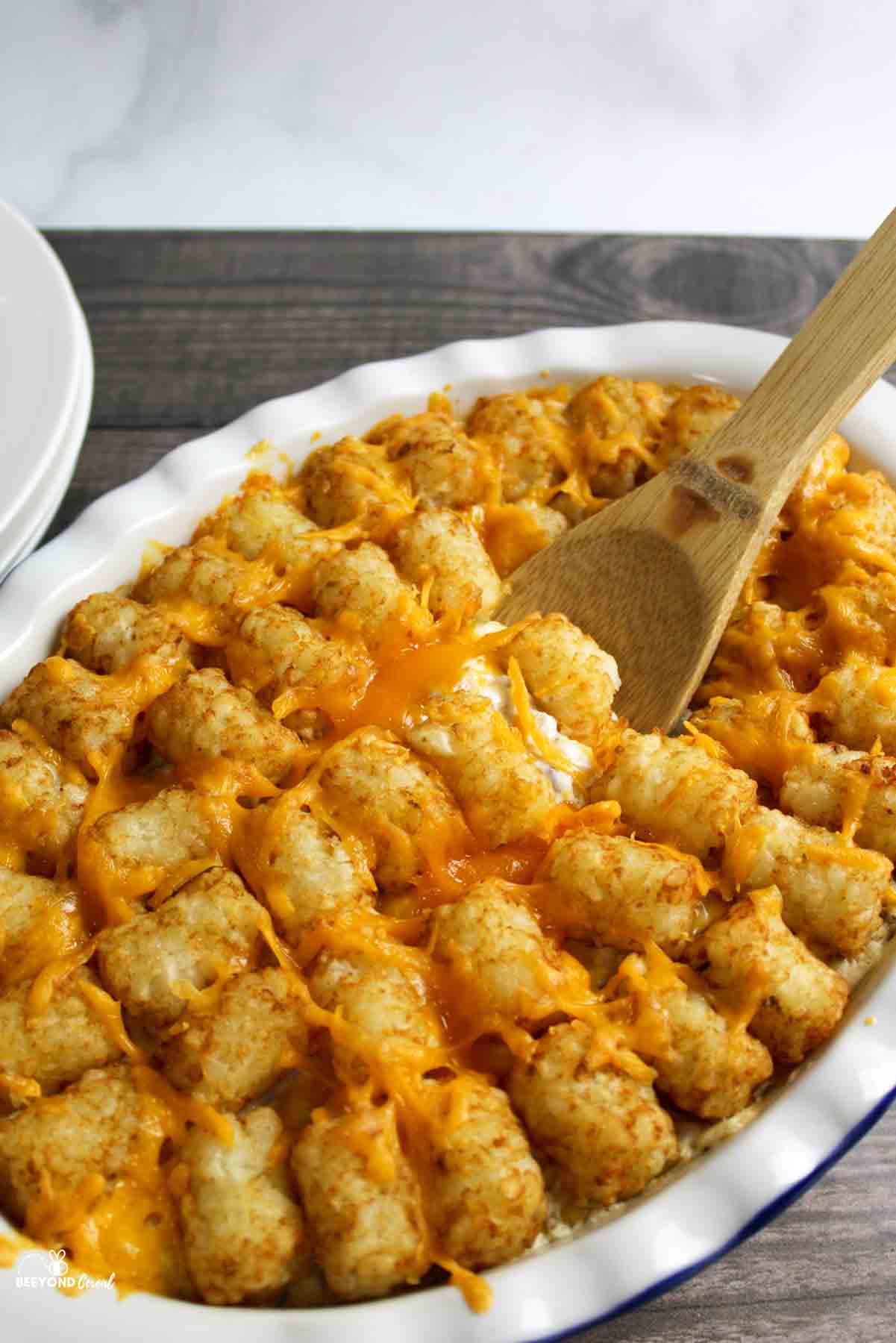 a wooden spoon sticking into a dish filled with tater tot casserole.