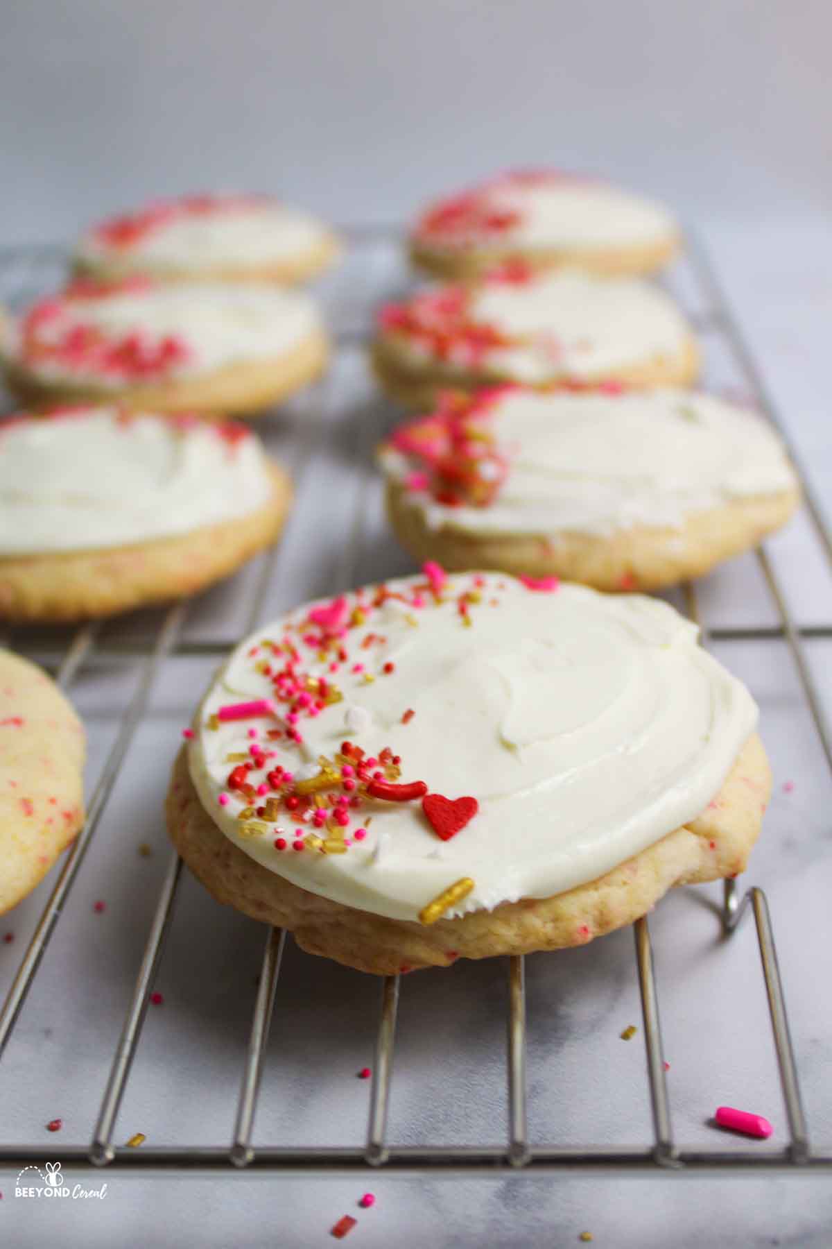 frosted and sprinkle covered cherry chip cookies on wire rack.