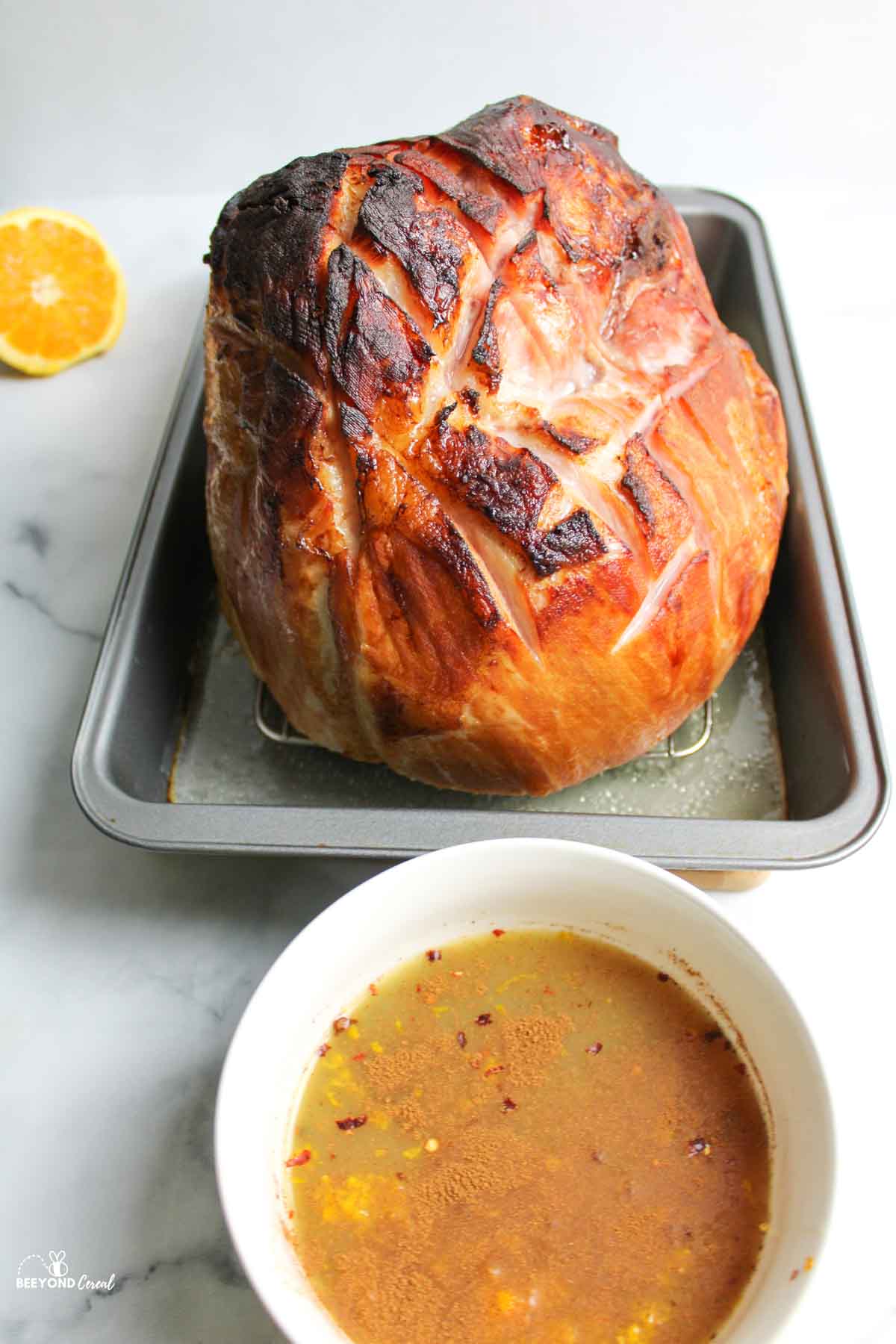 a baked ham in a pan with a bowl of honey orange glaze in front