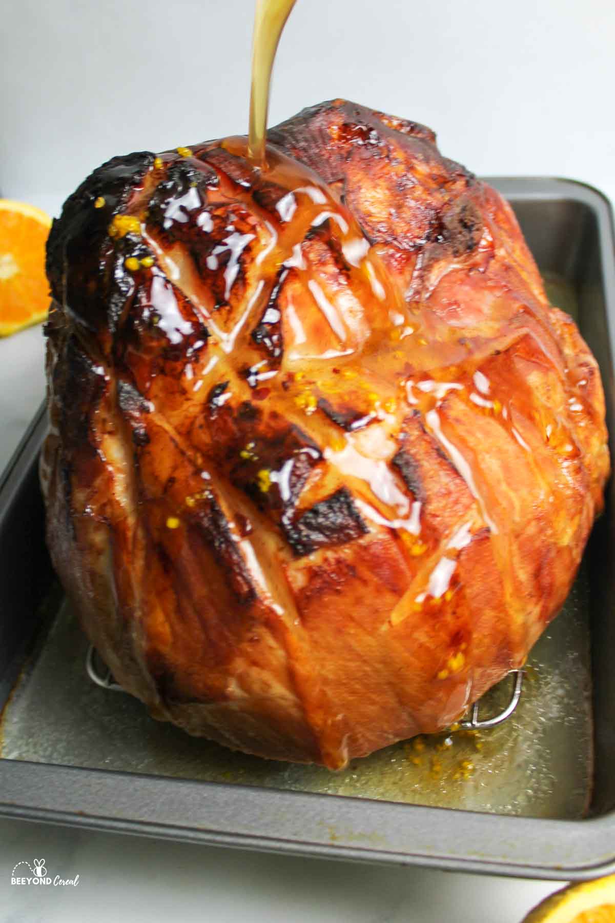 pouring the honey glaze sauce on the ham in a pan.