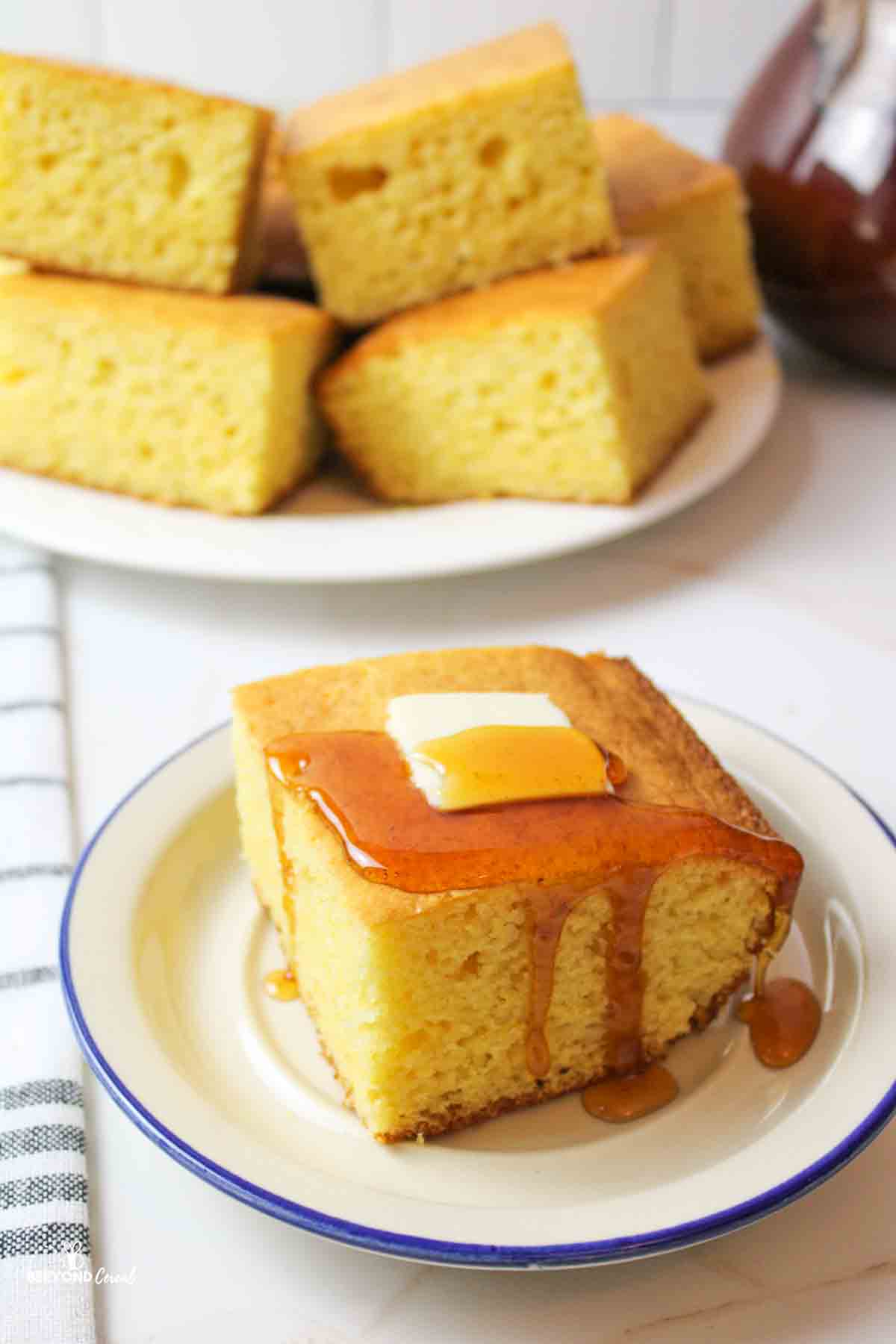 a slice of cornbread on a plate topped with a pad of butter and drizzle of honey