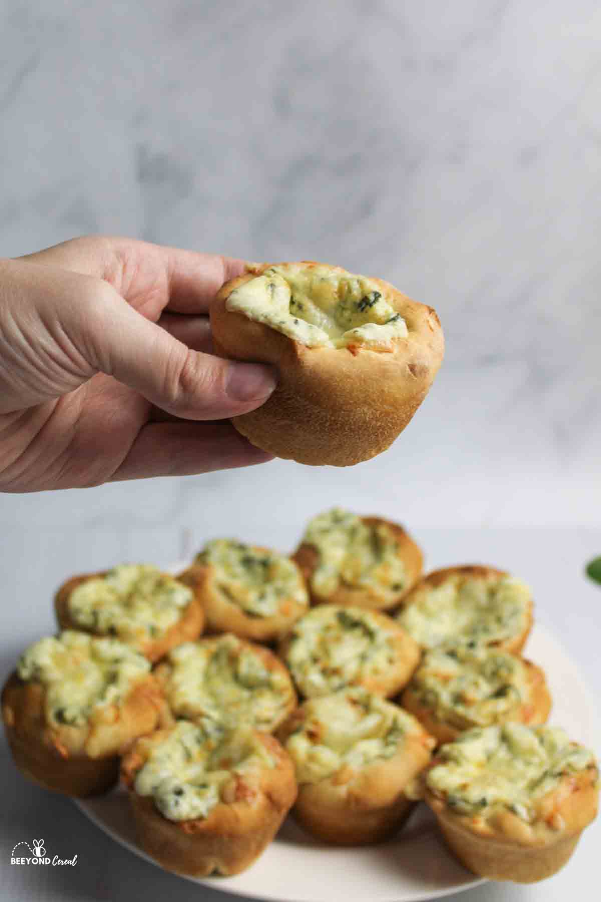 a hand holding up a spinach dip muffin.