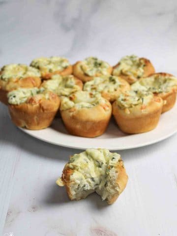 a plate of spinach dip muffins with one in front missing a bite