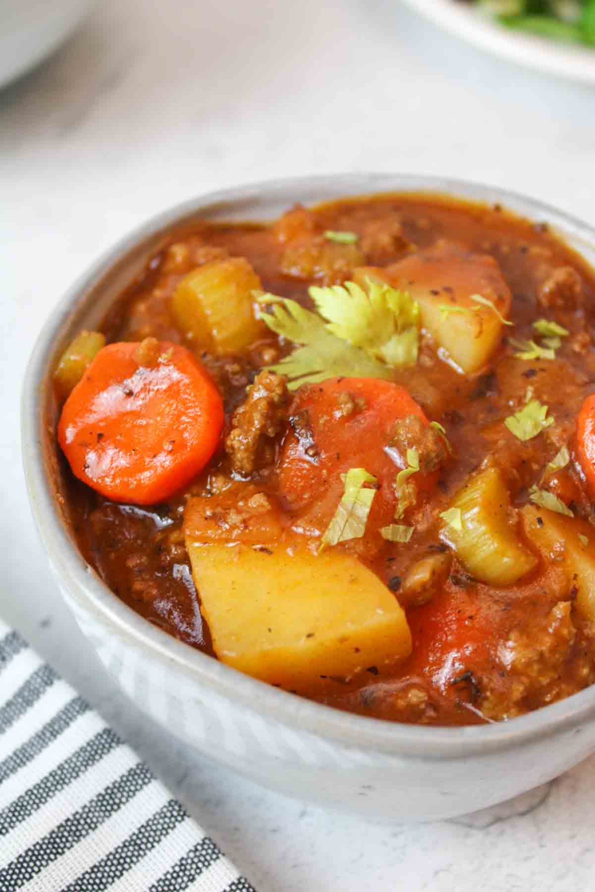 a bowl of stew with spoons and empty bowls to the sides.