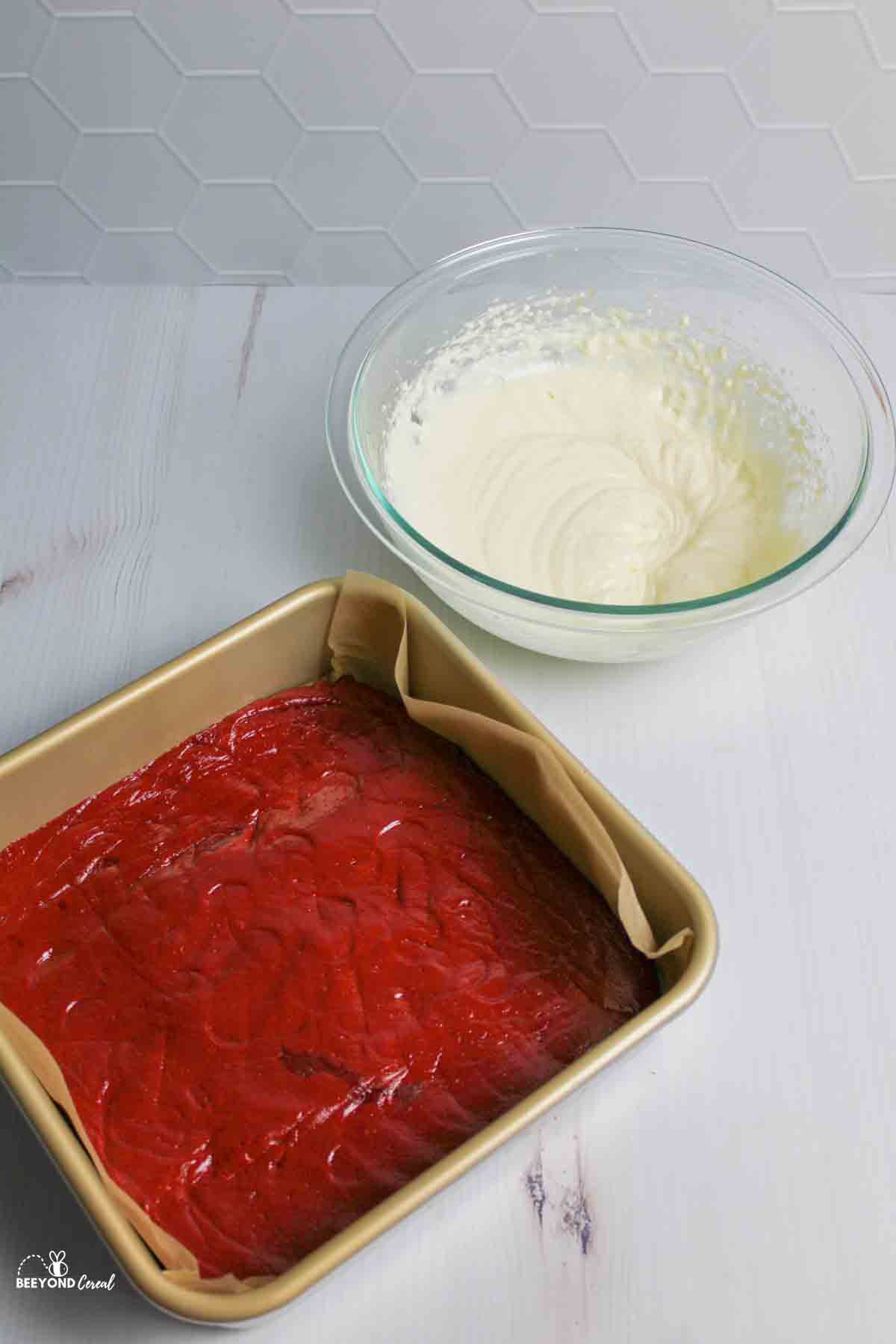red velvet brownie batter in pan with cheesecake mix in bowl