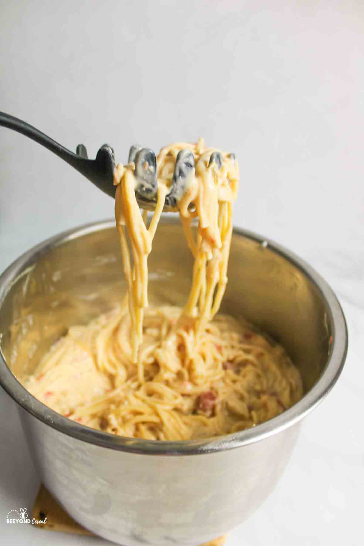 a pasta server holding up a scoop of instant pot chicken spaghetti above the stainless steel pot