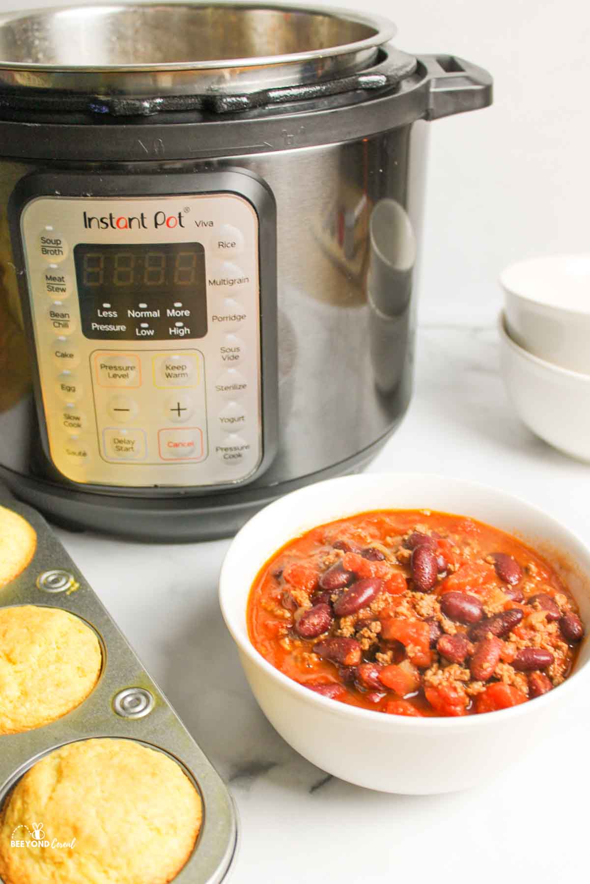 chili in a bowl in front of instant pot and next to tray of cornbread muffins