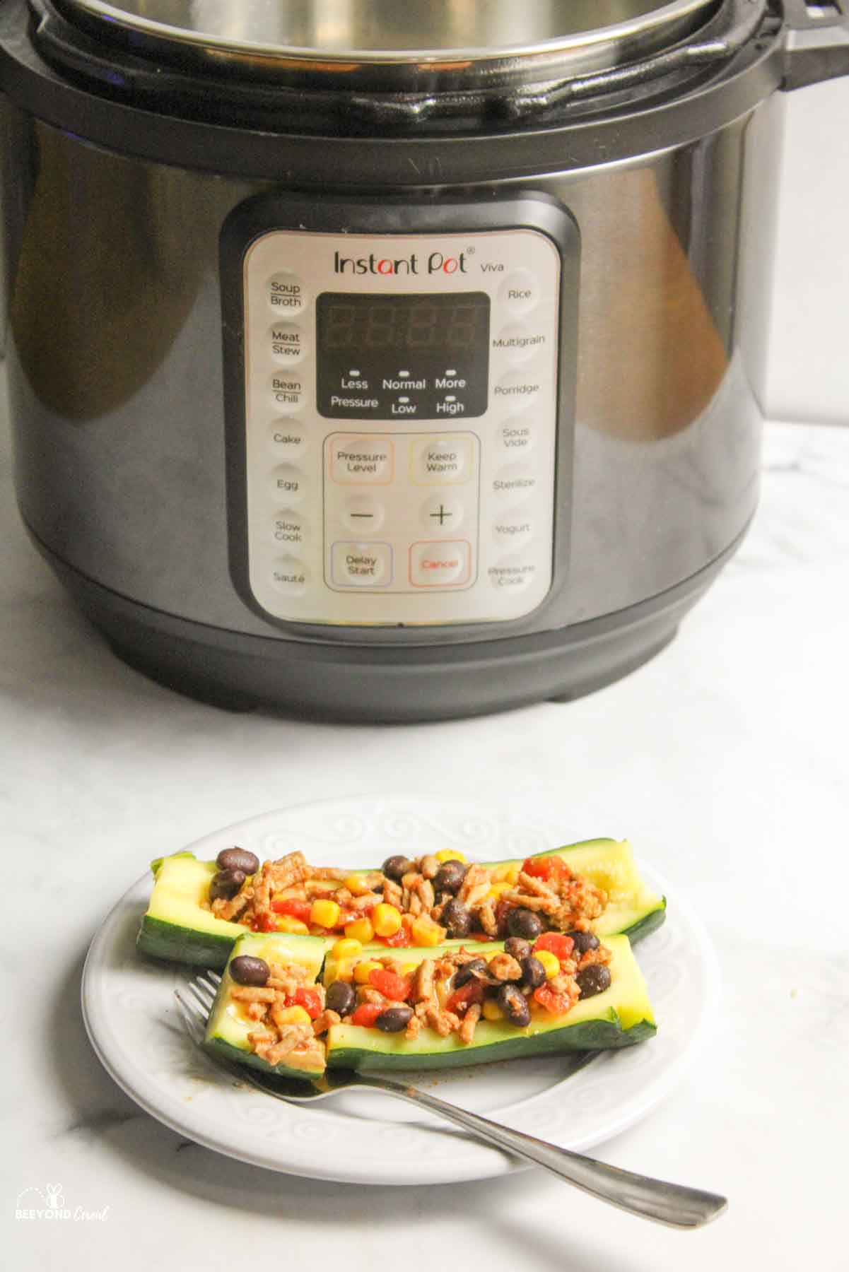 two zucchini taco boats on a plate with a fork in front of an instant pot.