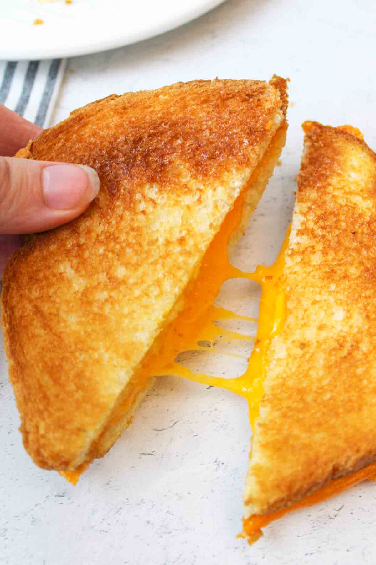 a hand pulling two halves of microwave grilled cheese apart to reveal gooey cheese center