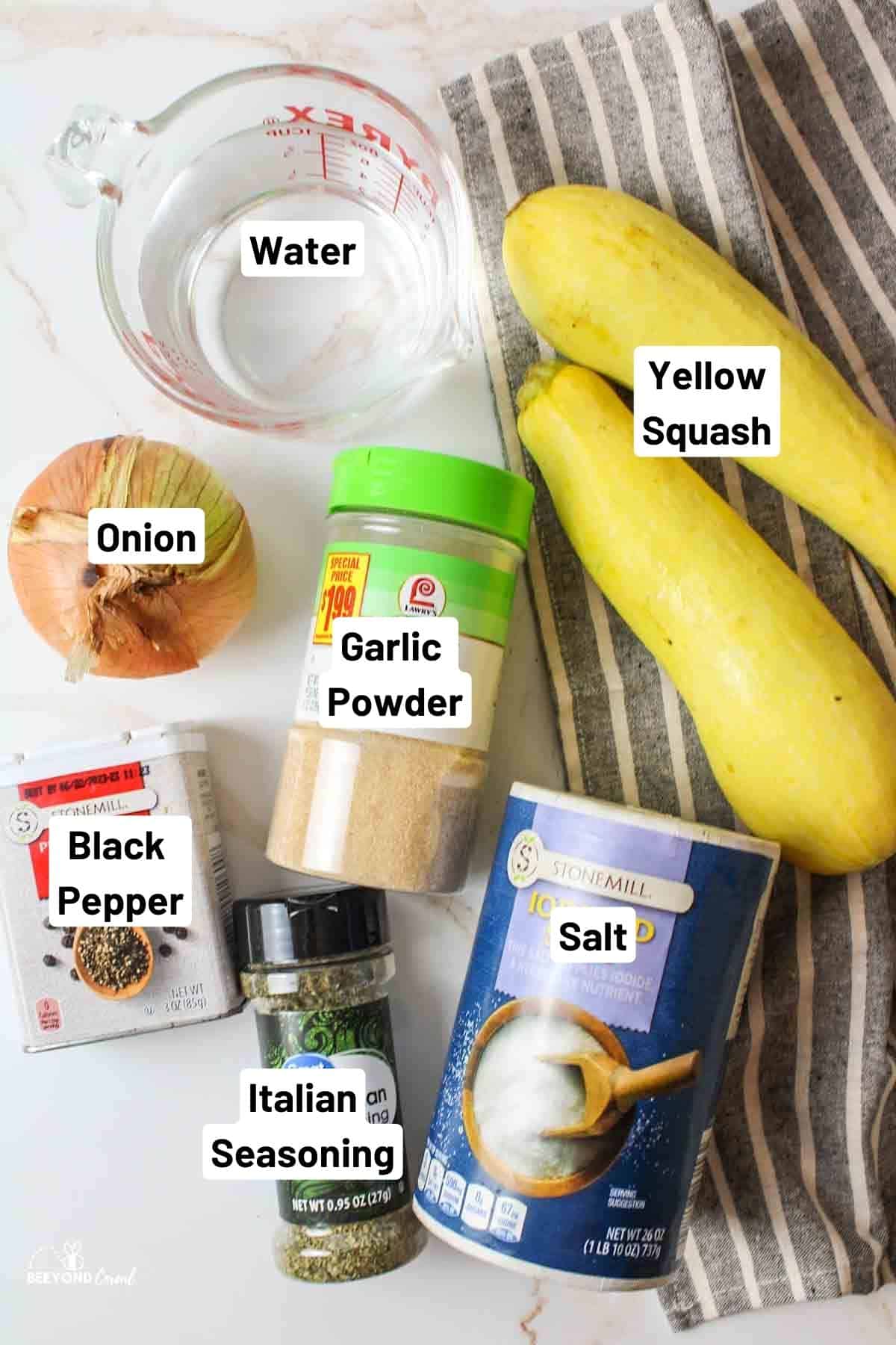 a covered bowl of yellow squash and onions next to a box of cling wrap and pitcher of water