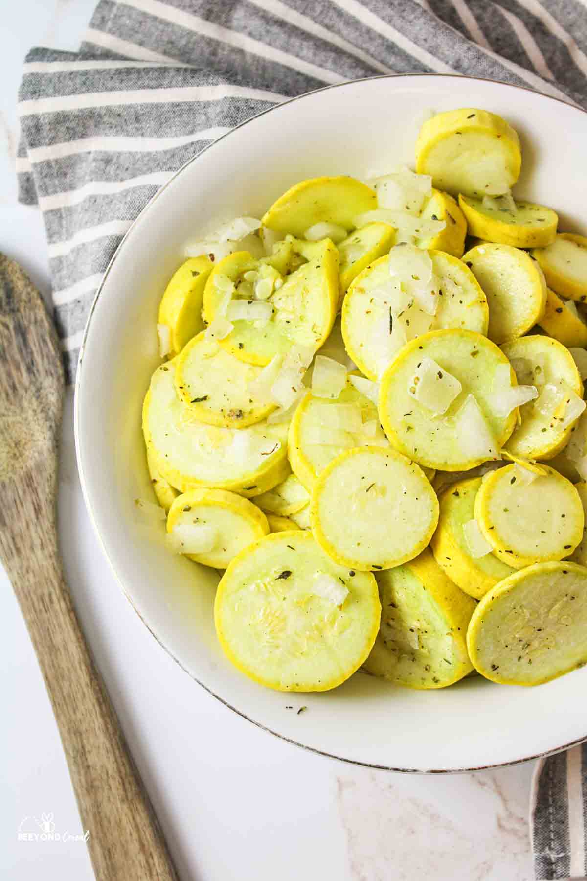 a large bowl filled with cooked yellow squash next to a wooden serving spoon.