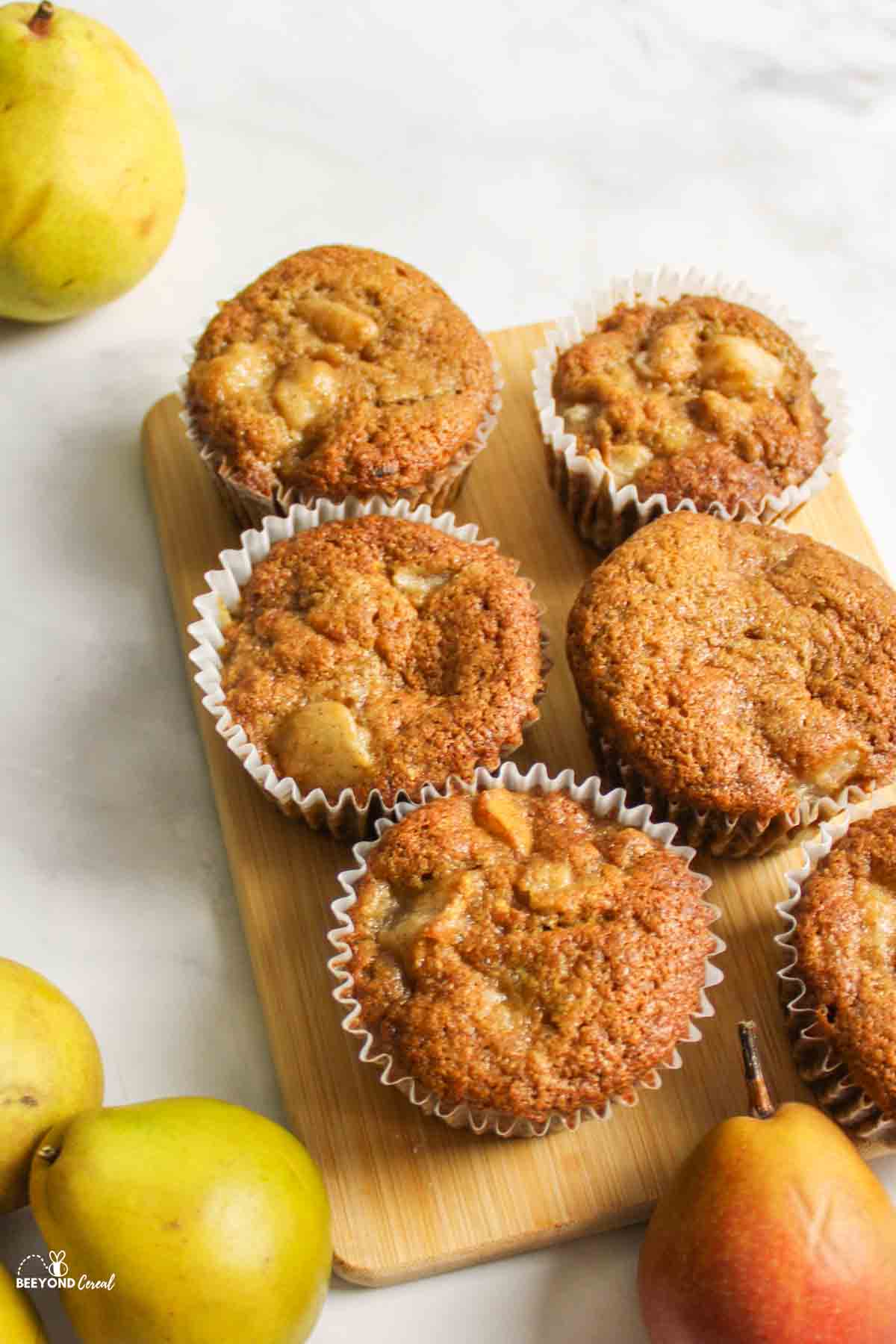 several pear muffins on wooden board surrounded by fresh pears