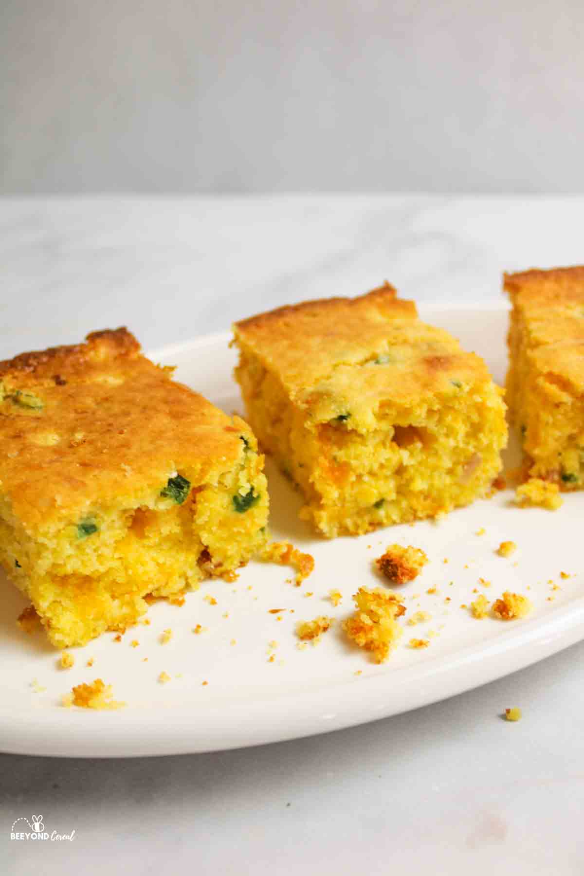 three squares of jalapeno cornbread on an oval plate.