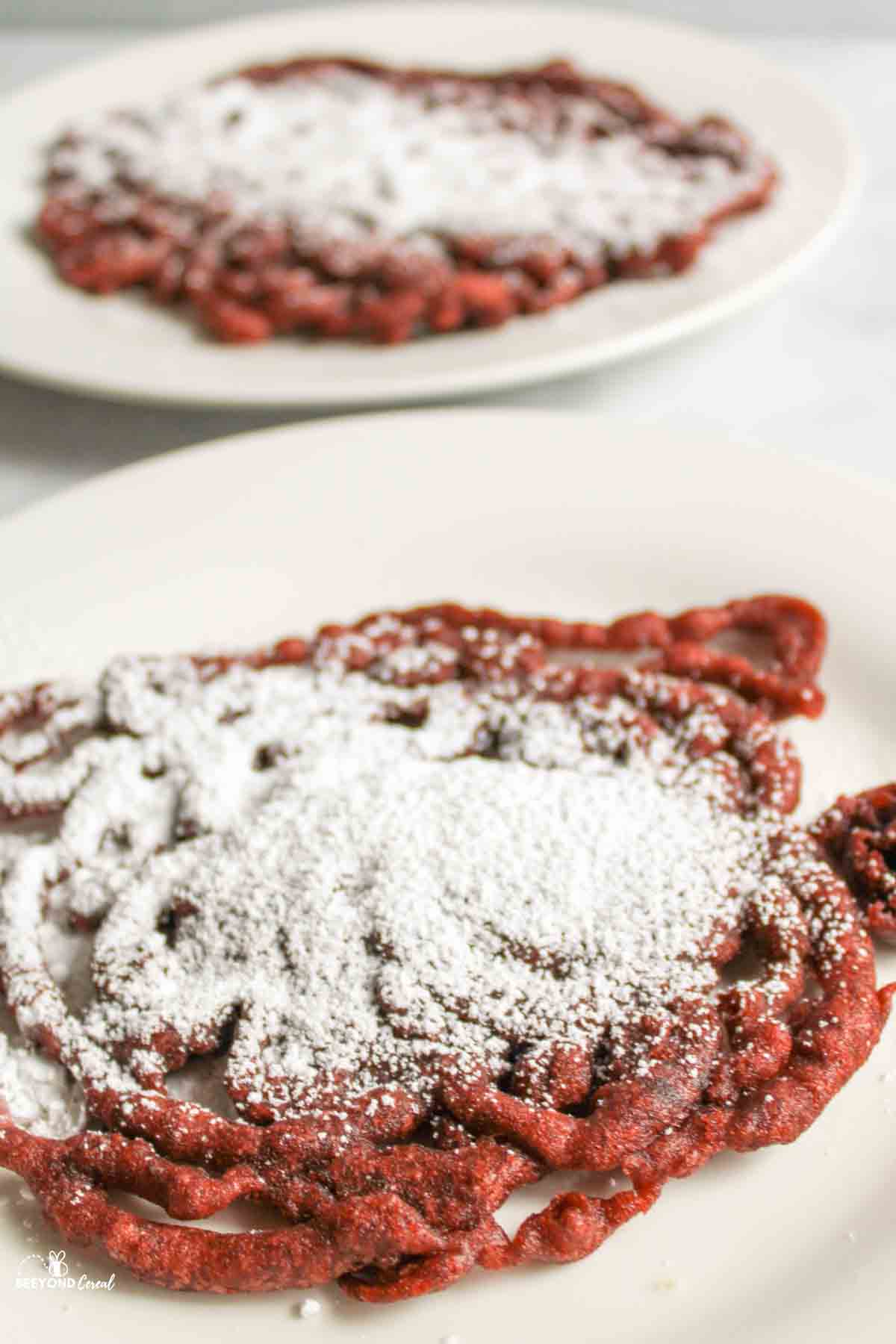powdered sugar covered funnel cakes on white plates.