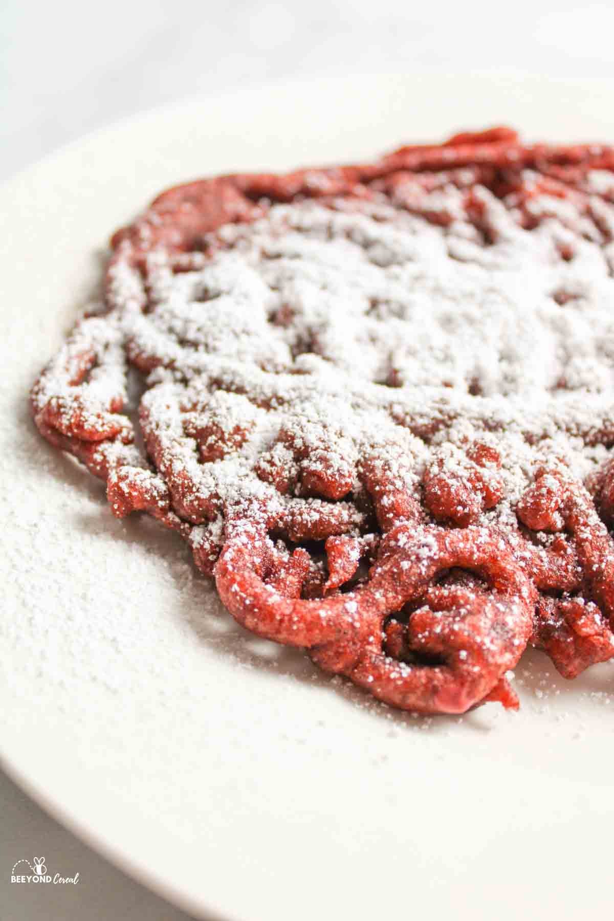 side view of a plate with red velvet funnel cake and powdered sugar on top