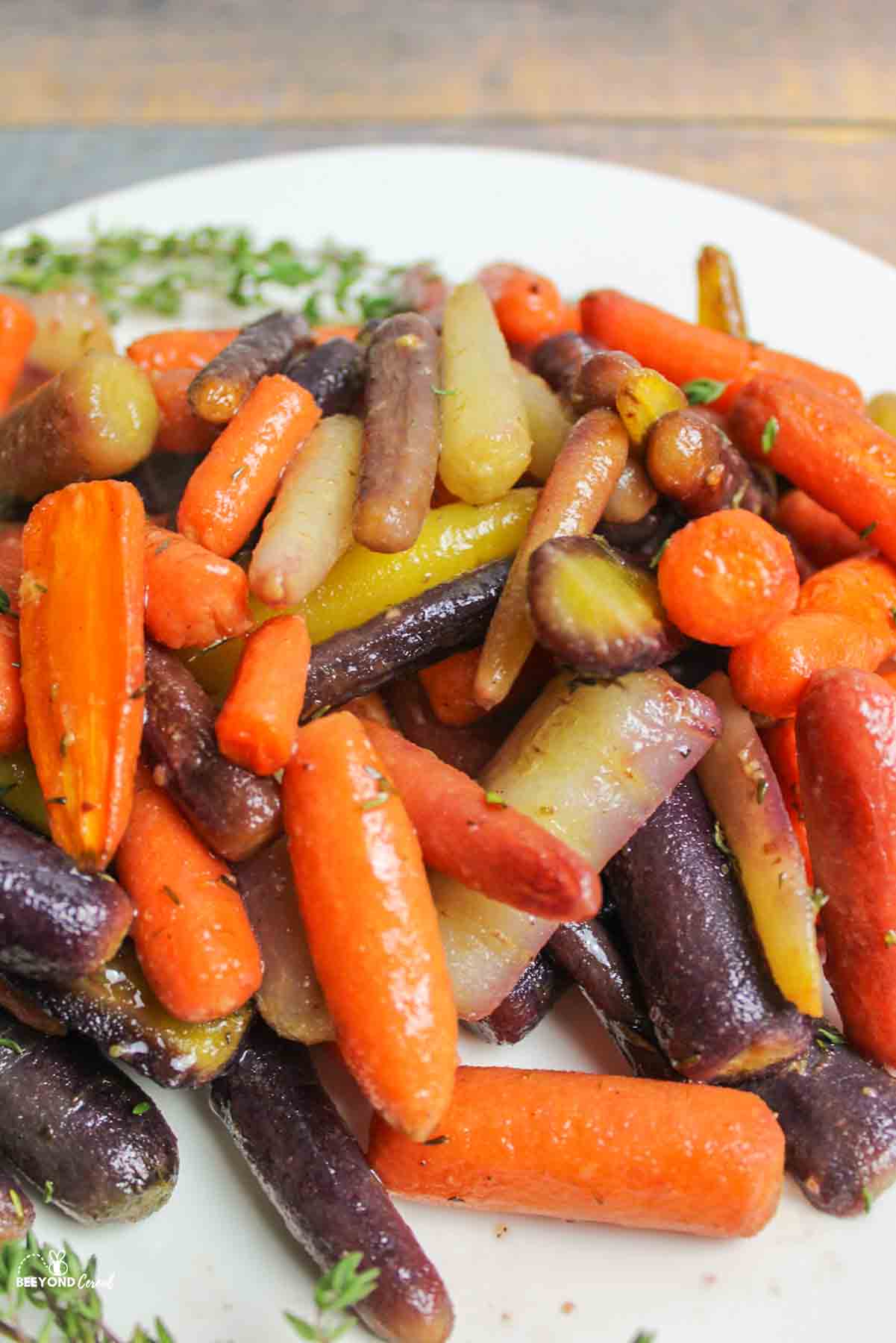 an upclose view of roasted rainbow baby carrots on a plate with fresh thyme