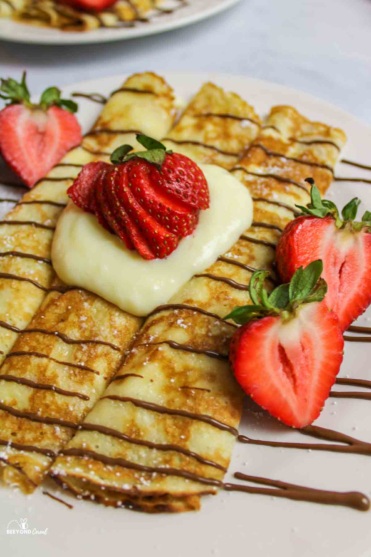 pancake mix crepes rolled on a plate with custard and fresh strawberries.