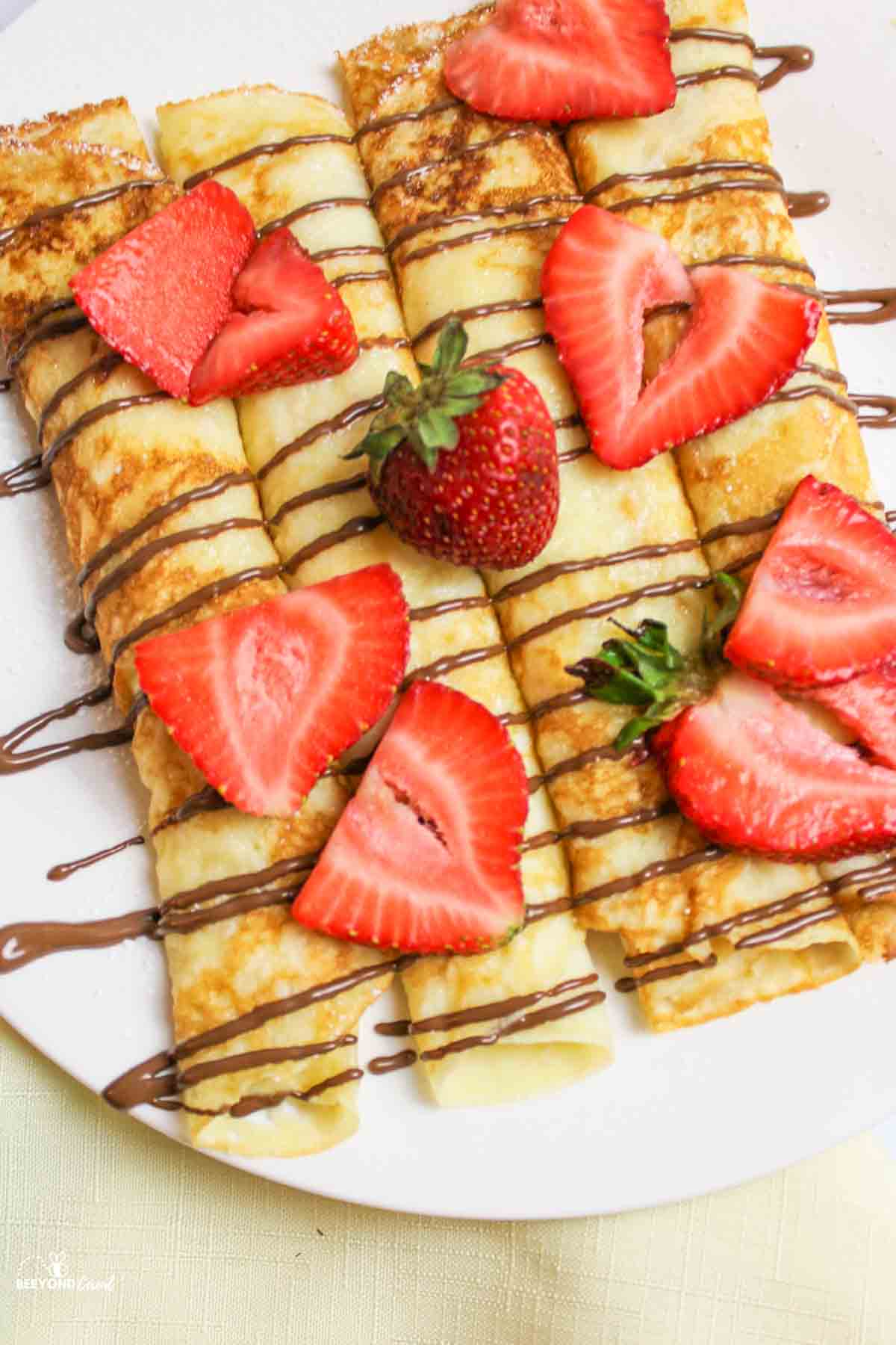 aerial view of crepes on a plate with chocolate drizzle and fresh strawberries