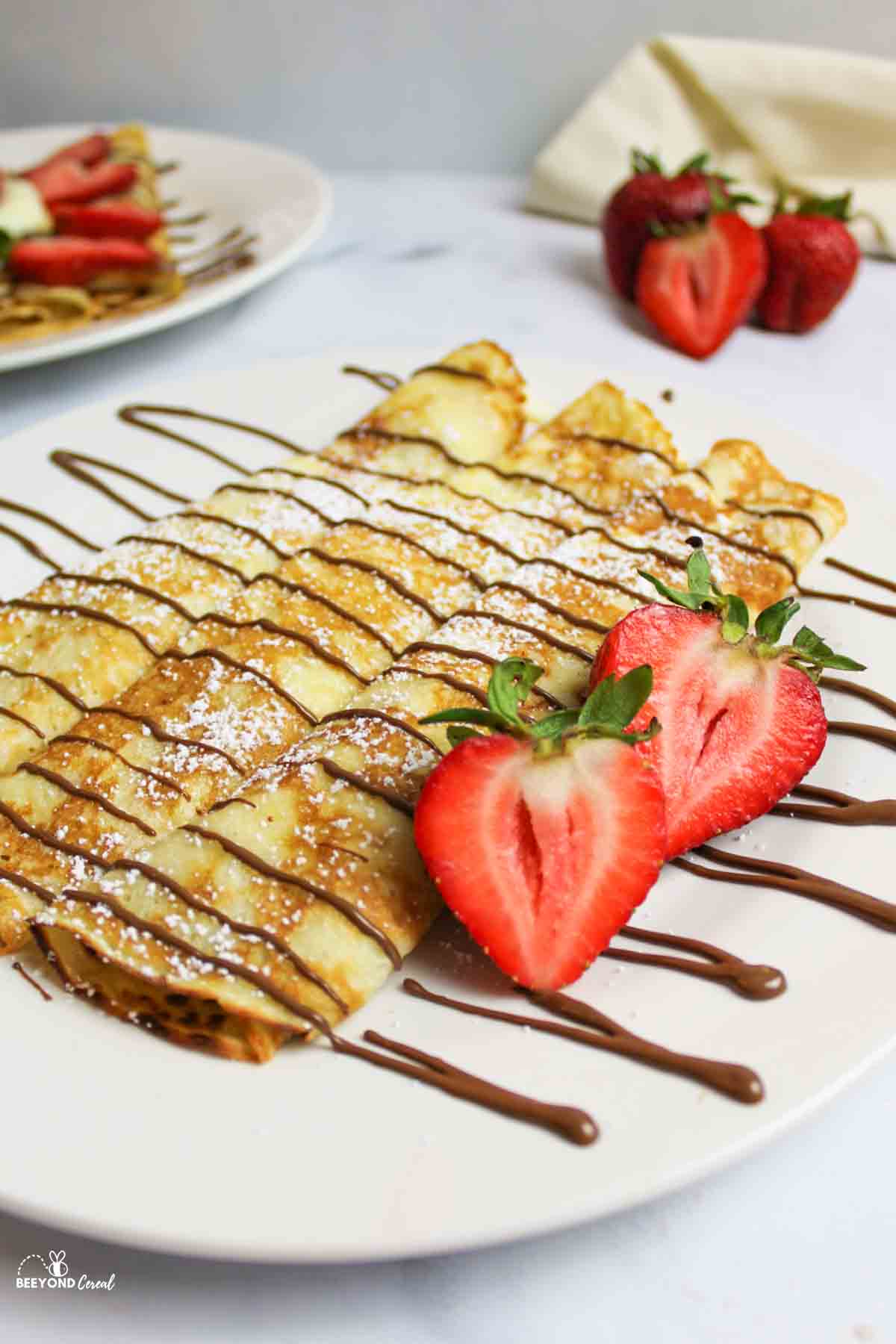 pancake mix crepes rolled on a plate with chocolate drizzle powdered sugar and fresh strawberries.
