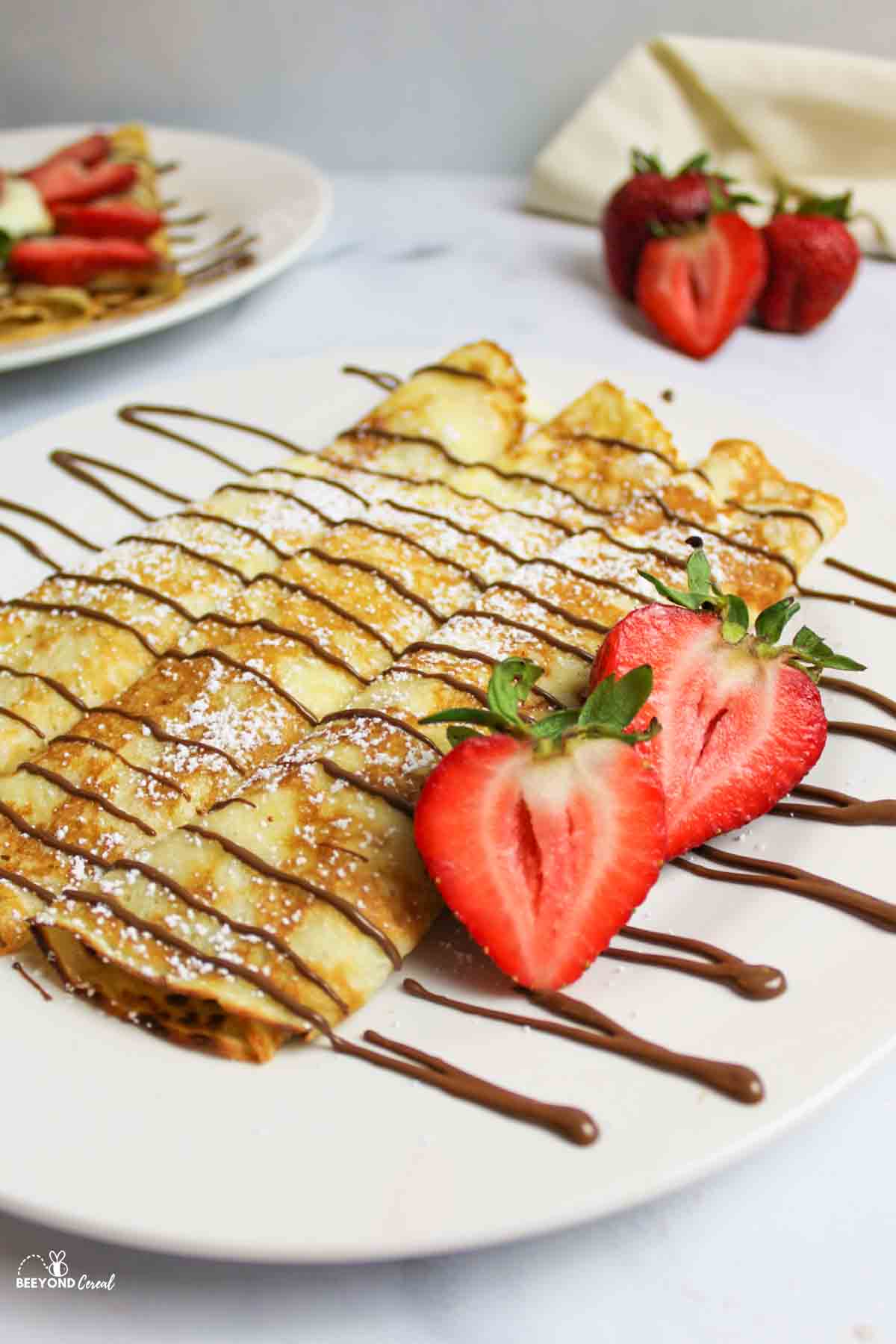 Pancake mix crepes rolled on plate with chocolate drizzle, powdered sugar, and strawberries.