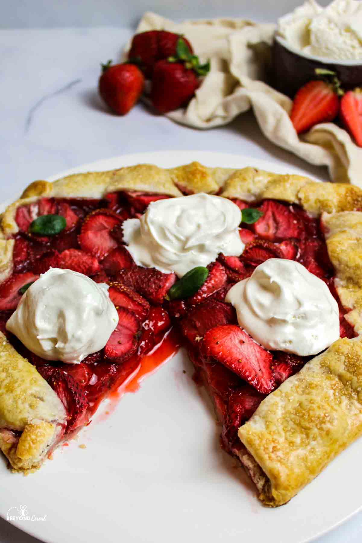 a sliced strawberry galette with three dollops of whipped cream on top.
