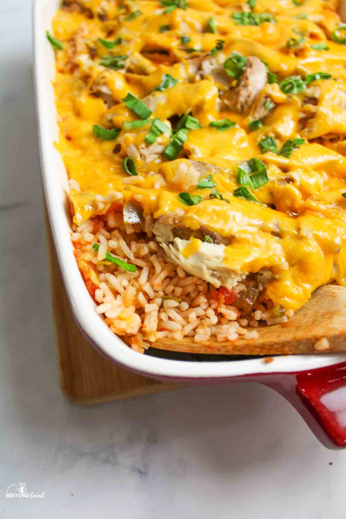 Wooden spoon scooping salsa rice and cheesy chicken from baking dish.