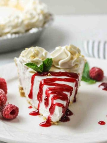 a turned slice of cheesecake on a plate with halved strawberry to the side and a strawberry glaze on top.