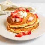 a stack of cheesecake pancakes with a dollop of cream cheese on top and diced strawberries scattered over the top