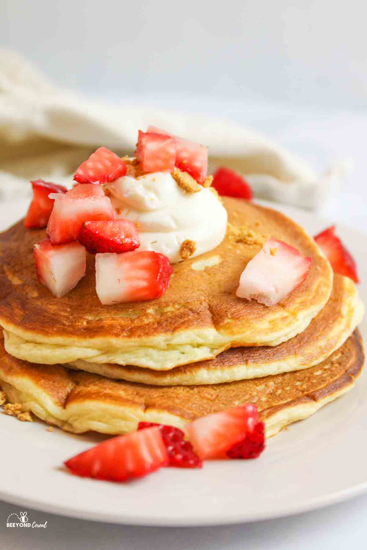 fresh diced strawberries and cream cheese dollop on a stack of cheesecake pancakes
