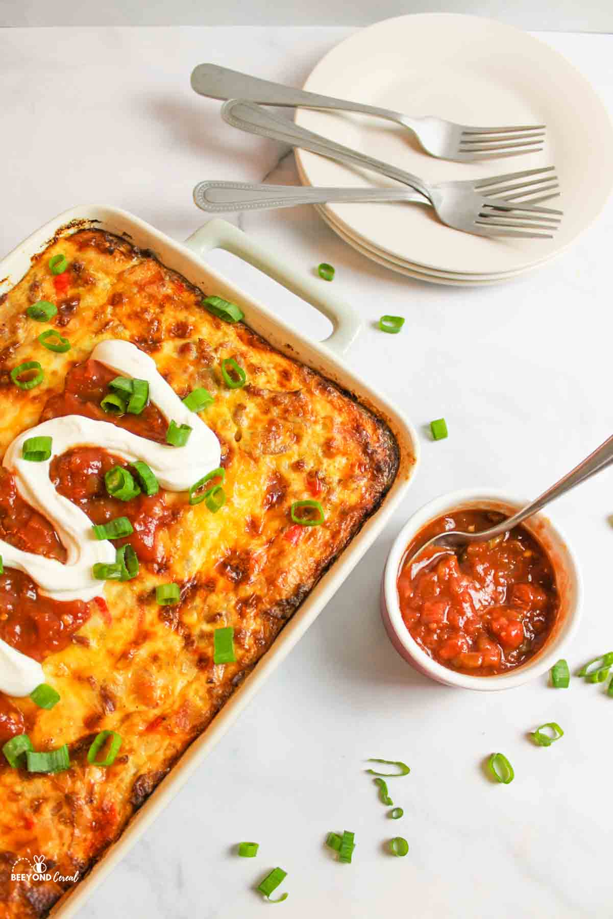 a baking dish of garnished tater tot casserole with a bowl of salsa and spoon to the side.