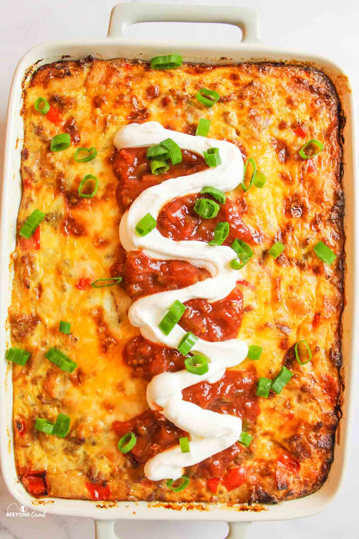 a baking dish filled with tater tot casserole and topped with sour cream, salsa, and green onions.