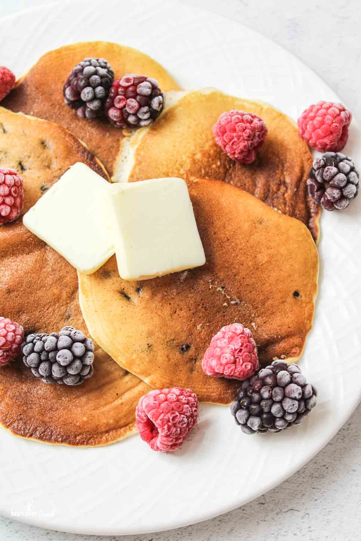 muffin mix pancakes on a plate topped with frozen berries and pads of butter.