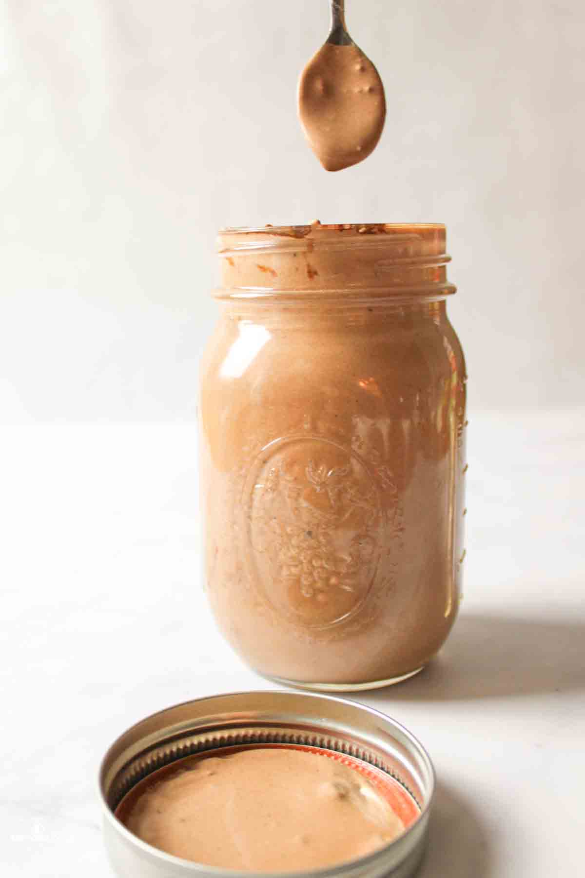 a spoon hovering over a mason jar of chocolate ice cream mixture seeing if the liquid will drop off of the spoon