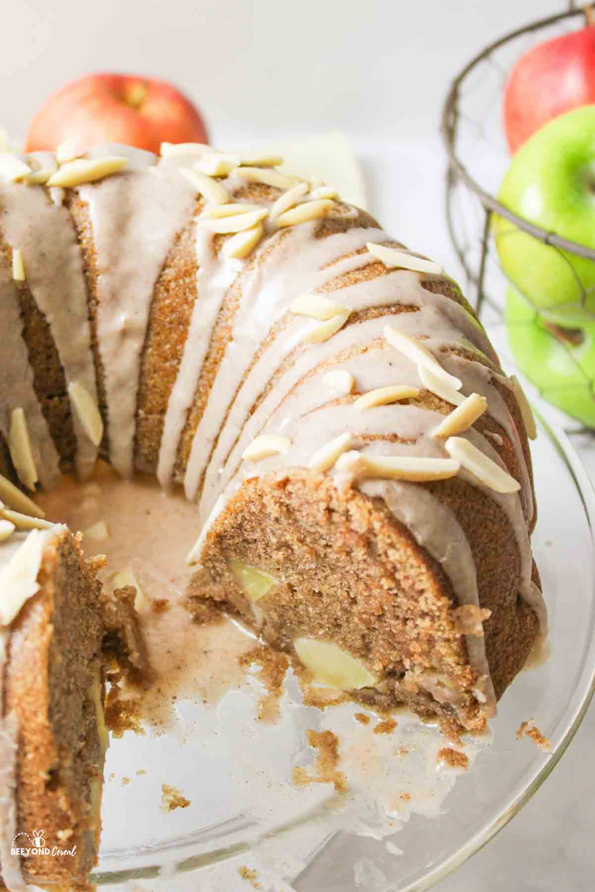 a sliced apple bundt cake with glaze and fresh apples in the background