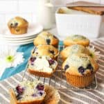 blueberry muffins on a cooling rack with one split in half and topped with some butter.