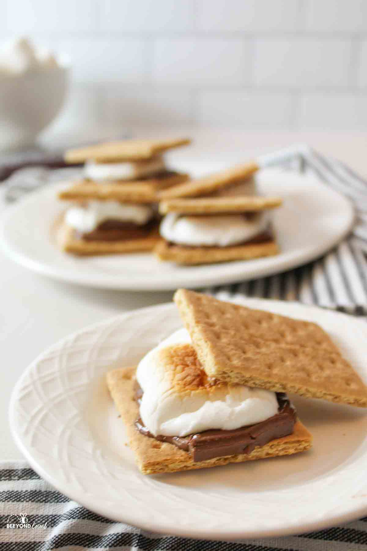 an angled view of a broiled smore with the top graham cracker off to the side to show the toasty marshmallow underneath and more smores in the background