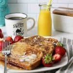 an upclose view of french toast on a plate with fresh strawberries and coffe and orange juice in background