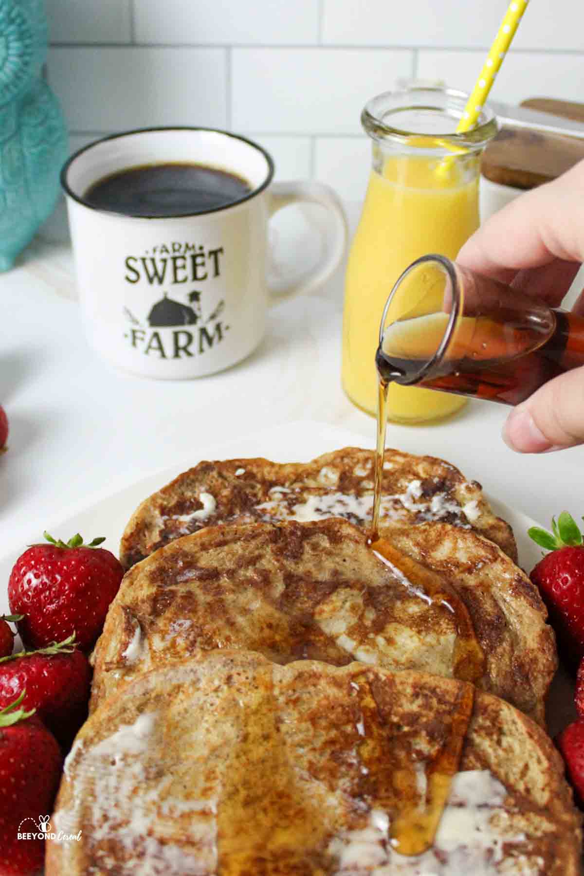 a hand pouring some syrup over the top of french toast.