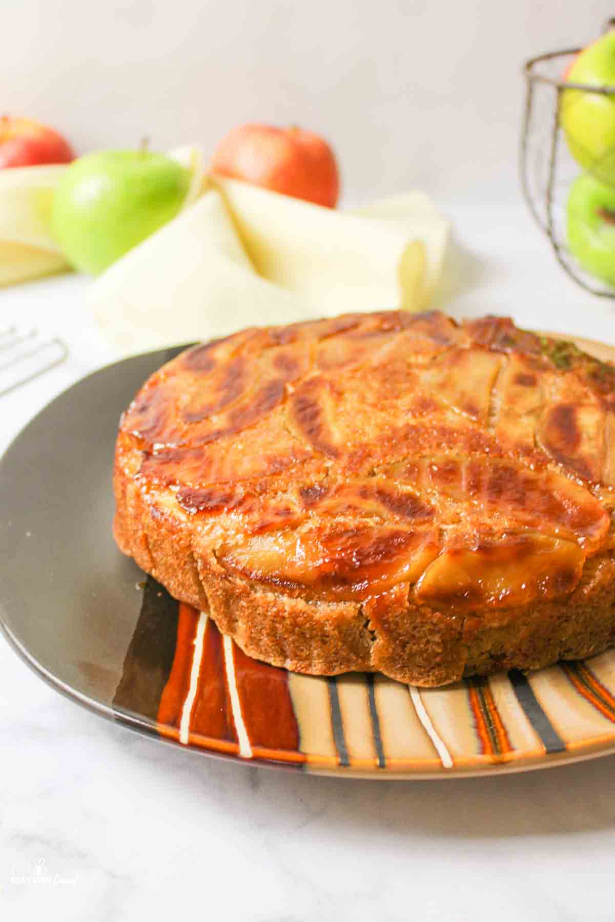 a single layered vegan apple upside down cake on a brown striped plate.