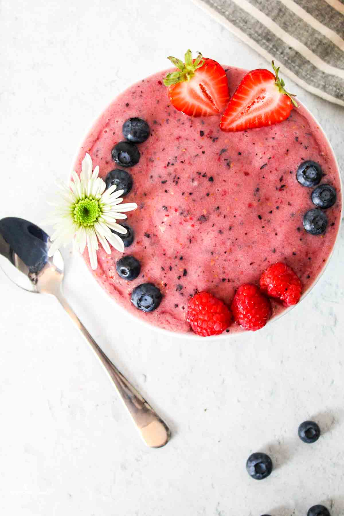 aerial view of watermelon smoothie bowl with fruits and a flower on top and spoon to the side