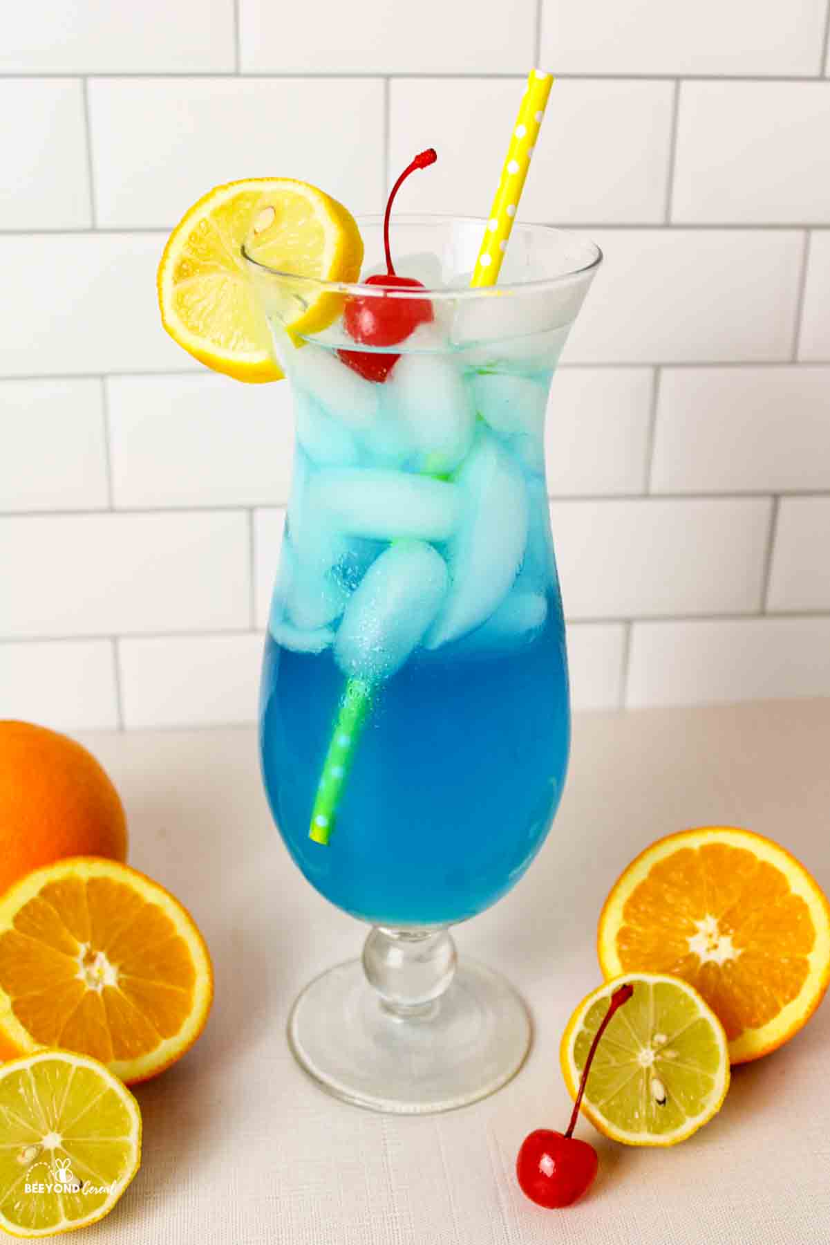 Glass of blue lagoon mocktail with ice, lemon slice, cherry garnish.